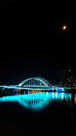 Illuminated bridge against blue sky at night