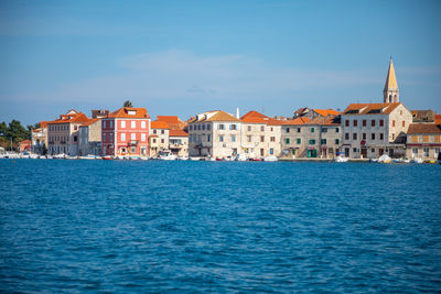 View of buildings by sea against blue sky