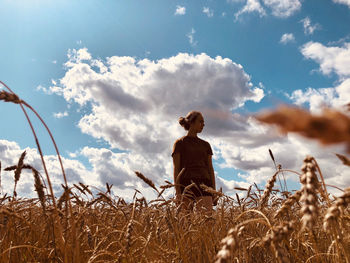 Teenage girl standing at wheat farm against cloudy sky