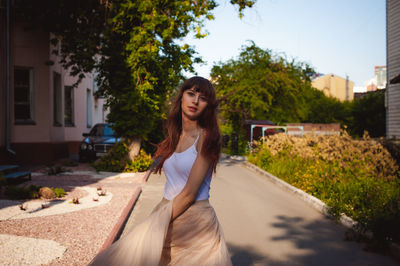 Portrait of young woman standing on road against trees