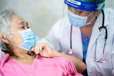 Doctor wearing mask and face shield talking with patient at hospital