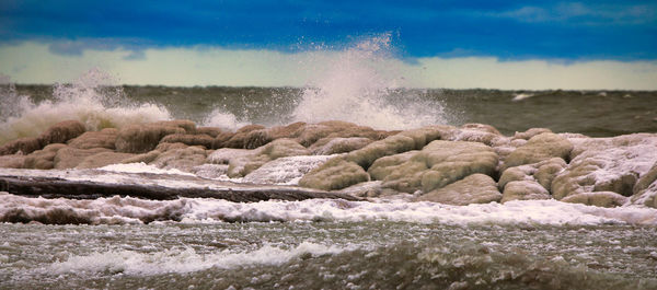 Waves splashing on rocks at shore against sky