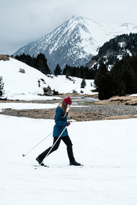 Side view of unrecognizable lady in warm clothes skiing on snow on background of mountain ridge