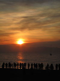 Silhouette people standing on beach against sky during sunset