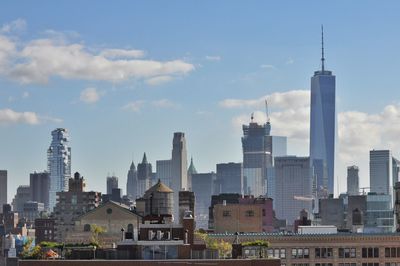 One world trade center by modern buildings against cloudy sky