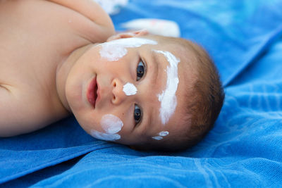 High angle portrait of baby with suntan lotion on face while lying on beach towel