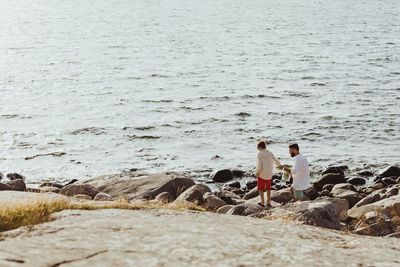 Rear view of father holding hands with son while standing by sea on rocks