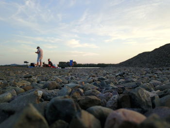 People on rocks at beach against sky during sunset