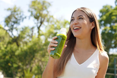 Portrait of young woman drinking water while standing outdoors