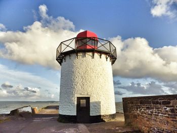 Lighthouse on sea against cloudy sky