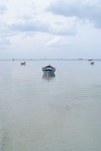 Boats in calm sea against cloudy sky