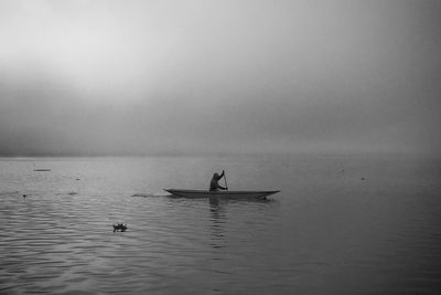 Person sailing boat on lake against sky