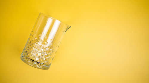 A mixing glass on a bright yellow background