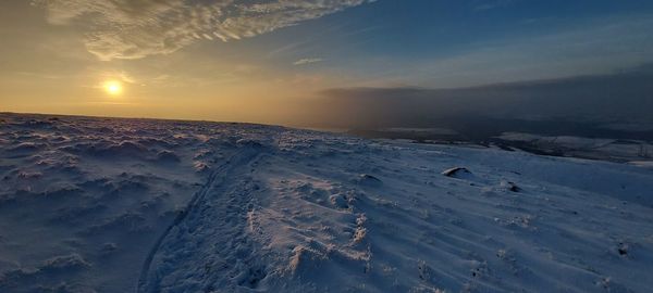 Snow covered landscape against sky during sunset