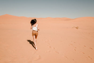 Woman on sand dune in desert against clear sky