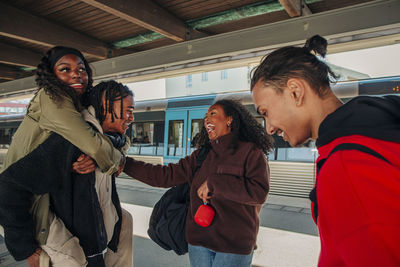 Young woman laughing while looking at playful friends at railroad station