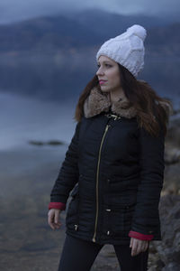 Beautiful woman looking away while standing by lake during winter