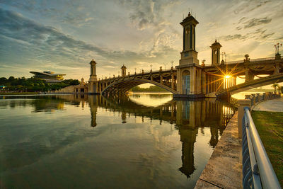 Arch bridge over river in city during sunset