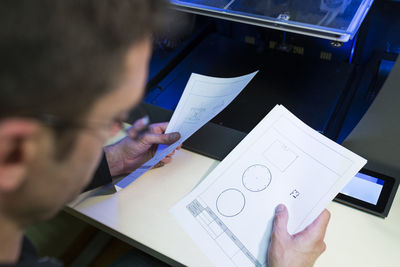 Engineer holding documents by 3d printer at table in office