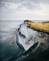 Scenic view of sea by mountain against sky