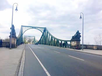 Road passing through city against cloudy sky