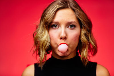 Close-up of woman blowing bubble gum against red background