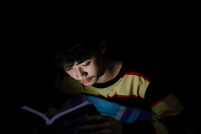Close-up of young man reading book in darkroom