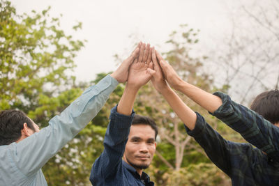 Friends with arms raised standing against sky in park