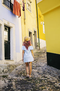 Rear view of young woman walking at alley amidst buildings