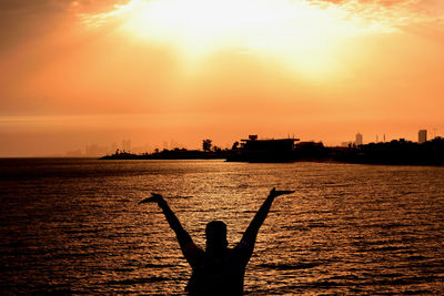 Silhouette person in sea against sky during sunset