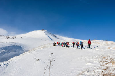 People on snowcapped mountain against blue sky