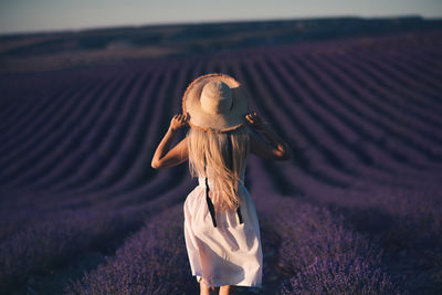 Rear view of girl wearing hat standing on flower field