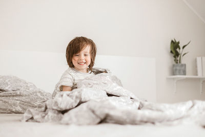 An adorable boy, toddler, plays on the parents' bed. sits wrapped in a blanket and laughs. 