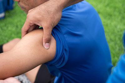 Cropped hands of male physical therapist rubbing soccer player shoulder on field