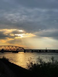 Silhouette bridge over river against sky during sunset