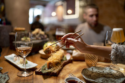 Woman using chopstick for picking up food with man sitting in background at restaurant