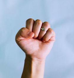 Cropped image of person with clenched fist wearing ring against sky