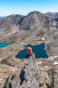 Rear view of woman sitting on rock by lake