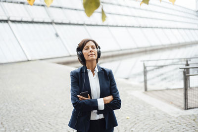 Female entrepreneur with arms crossed listening music outside office building