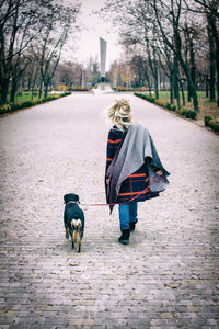 Rear view of woman with dog walking on footpath