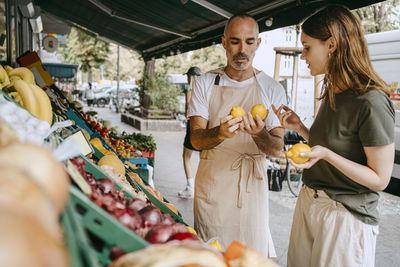Male vendor wearing apron while assisting female customer buying lemons at market