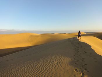 Man on sand dune in desert against sky