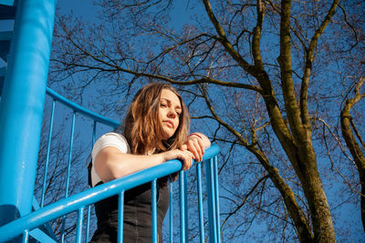 Full length of young woman on bare tree against blue sky