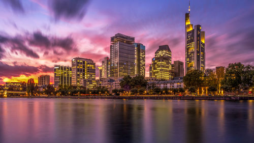 Illuminated buildings by river against sky at night