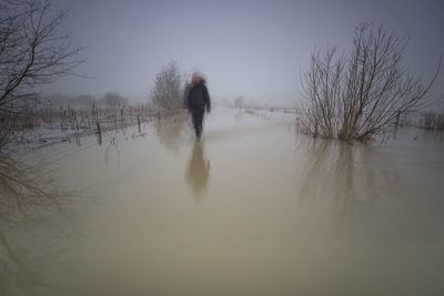 Blurred image of man walking on flooded field against sky