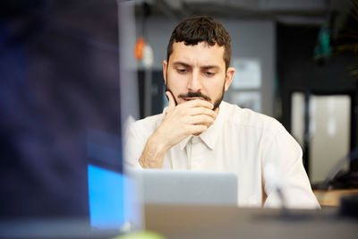 Stressed creative businessman looking at laptop while sitting in office