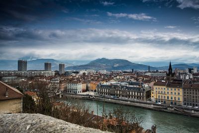 High angle view of buildings by river against cloudy sky