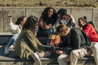 Happy man applying nail polish on hand of woman while sitting by cheerful friends in park