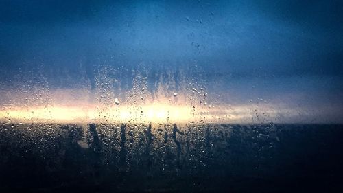 Close-up of wet window against sky during sunset