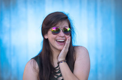 Portrait of happy woman wearing sunglasses while standing against wall